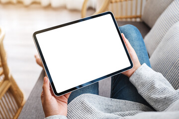 Mockup image of a woman holding black tablet pc with blank desktop white screen while lying on a sofa at home