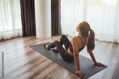Closeup image of a beautiful young asian woman sitting on training mat and do stretching to warm up before workout at home
