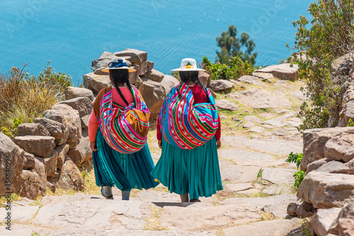 Two indigenous Peruvian Quechua women in traditional clothing walking down the steps to the harbor of Taquile Island, Titicaca Lake, Peru. photo