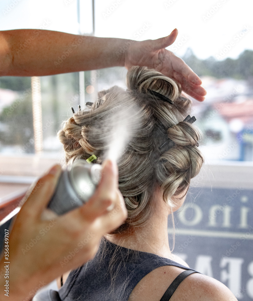 Naklejka premium Mulher cabeleireira aplicando spray laque no cabelo da sua cliente no salão de beleza