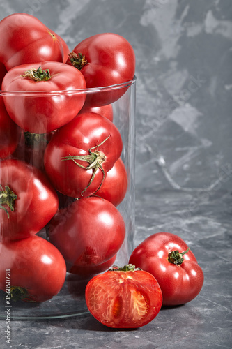 Fresh large tomatoes on a gray background. Whole and sliced tomatoes shot closeup with meta for text. Art concept tomatoes in the glass.
