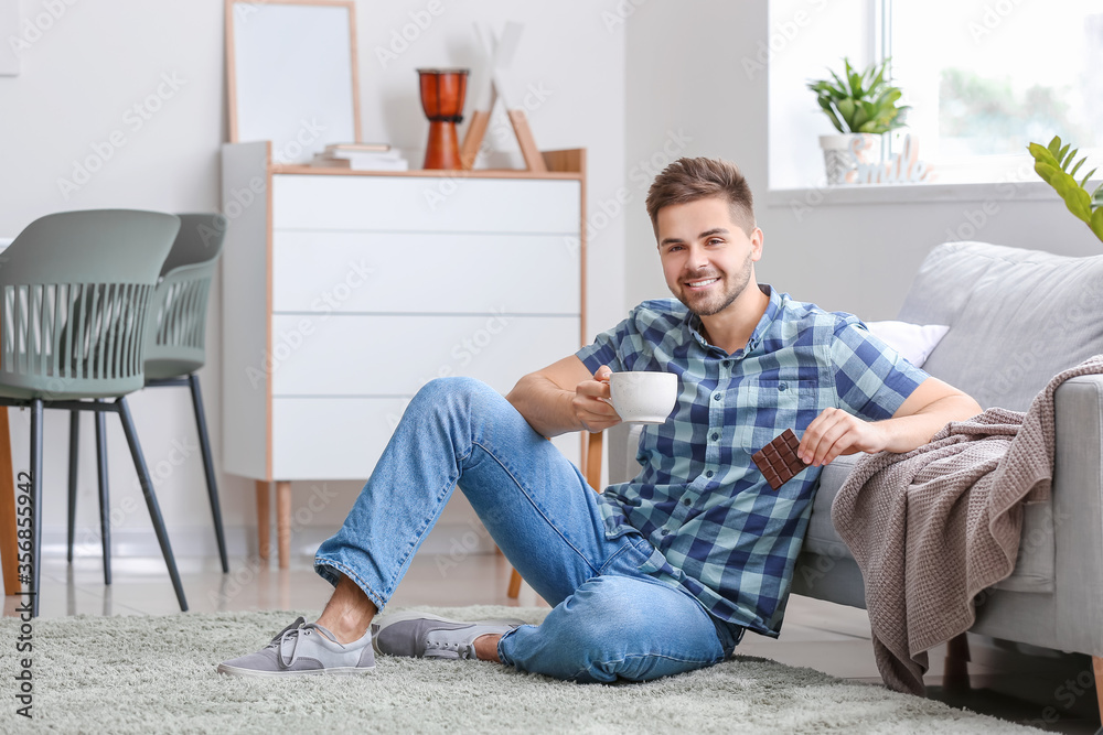 Handsome young man with tasty chocolate and cup of tea at home