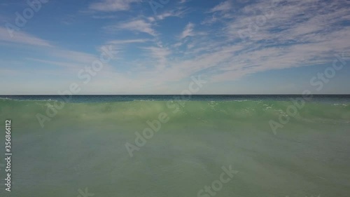Low drone flight towards incoming tidal ocean wave, rising up above water with panoramic view of blue sky, open sea, horizon as background and copy space.
