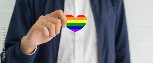 close up man hand holding rainbow heart shape for pride and lgbt concept