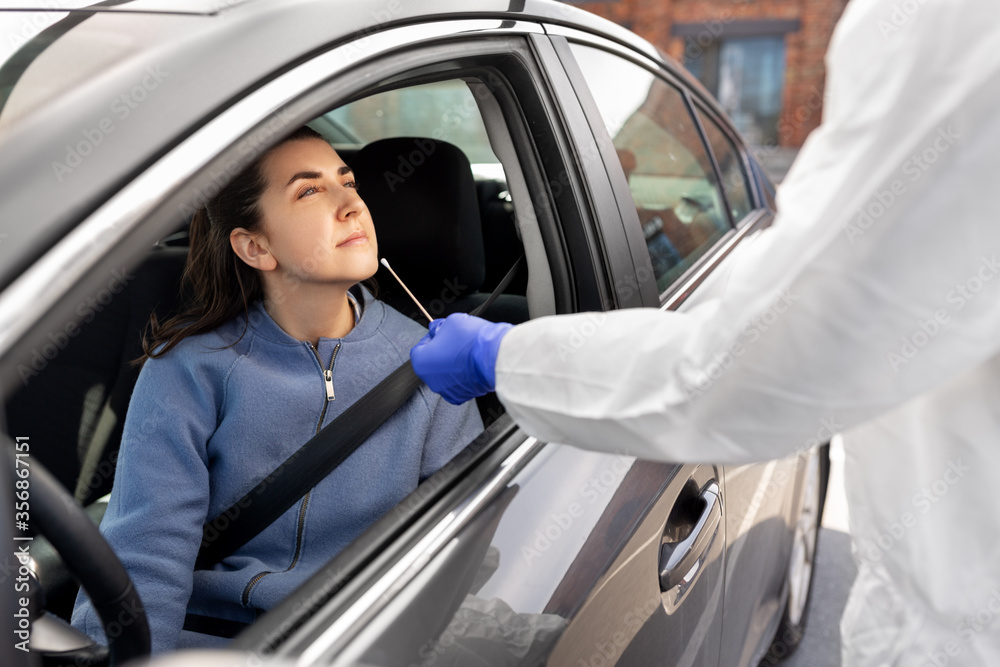 medicine, quarantine and pandemic concept - doctor or healthcare worker in protective gear or hazmat suit with cotton swab making coronavirus test for young woman in her car