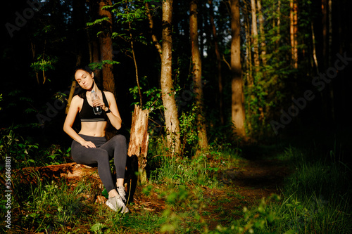 A beautiful girl is sitting in the forest to relax after drinking water, and also looks like she is thinking about some story.