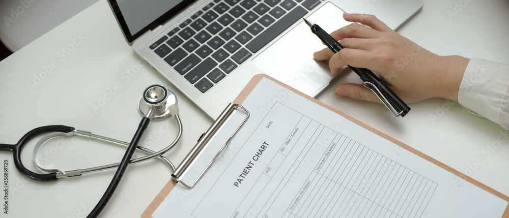 Doctor working with laptop, patient chart and stethoscope on worktable in examination room