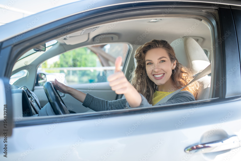 Satisfied smiling woman driving car showing ok