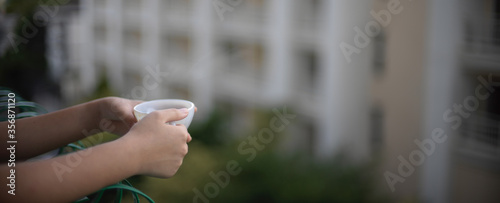A woman standing at balcony relaxing and holding morning coffee cup