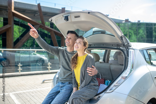 Man hugging woman near car pointing hand up