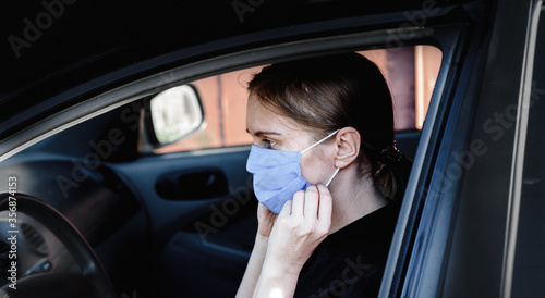 girl driving a car in a blue medical mask. virus protection, health care. worldwide pneumonia pneumonia pandemic.