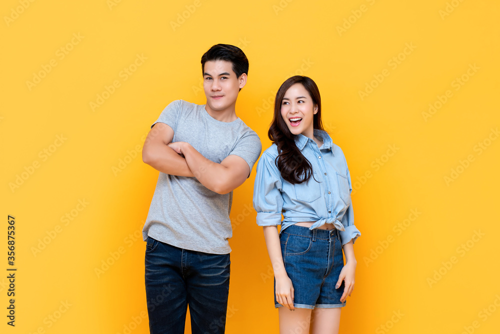 Timid smiling young Asian couple trying to be closer to each other isolated on yellow studio background Timid smiling young Asian couple trying to be closer to each other isolated on yellow studio background
