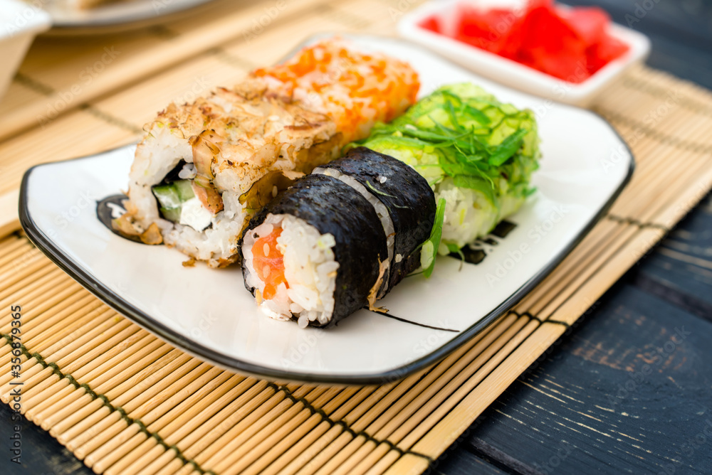 Several sushi on a white plate standing on a brown wooden background
