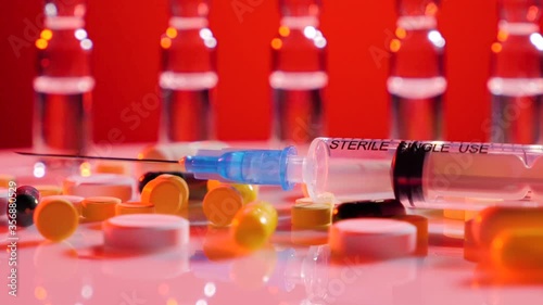 Ampoules for injection, syringe and many various pills rotate on a white surface over red background