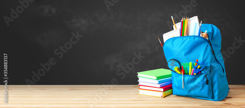 School bag. Backpack with supplies for school on the background of black blackboard. Copy space for text photo