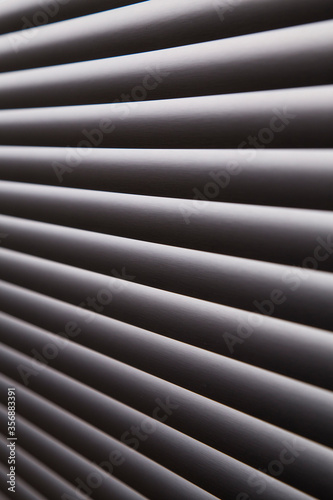 contrasty abstract close up filled frame background wallpaper shot of grey window blinds with rays of light shining through and leaving hard black shadows that create beautiful diagonal lines