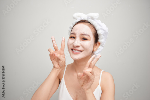 Young Asian woman applying facial clay mask over white background. Beauty treatments concept.