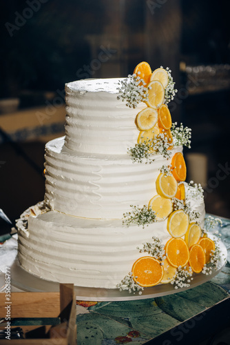 Large three-tier cake decorated with white cream and fresh citruses - slices of lemon and orange, wedding