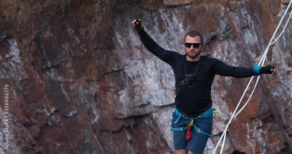 Close up of a man in glasses slacklining over a big pit, balancing, 4k