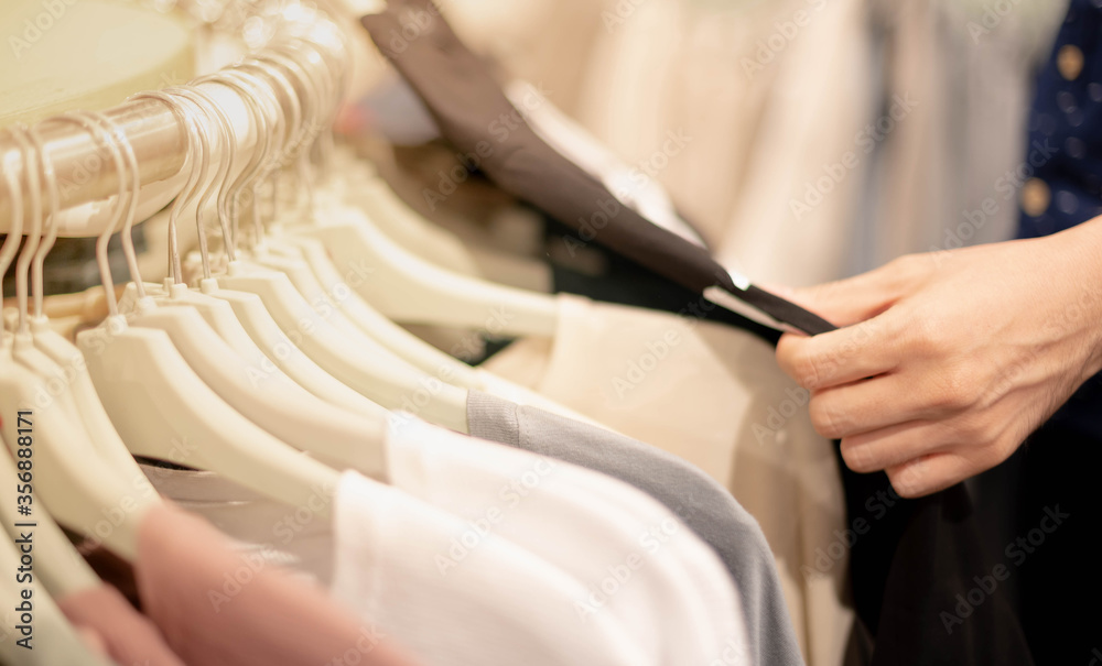 Male hand choosing clothes for checked pattern cotton shirt on the rack in cloth shop at department store.
