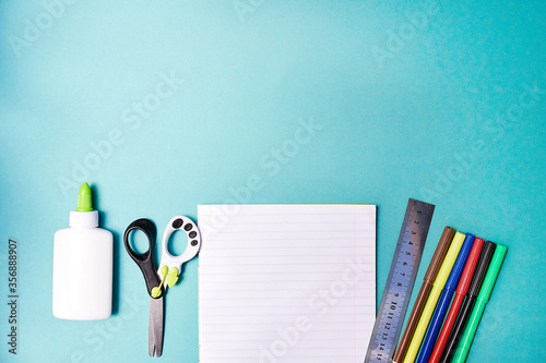 Exercise book, bright color markers, glue and line stationery on blue background. Back to school concept