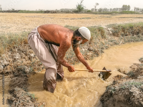 an Asian farmer is working in the fields with his tools and wearing Asian traditional clothes
