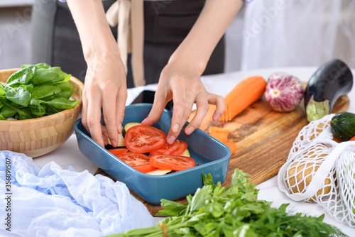 process of cooking vegetables with hands, tomatoes placed in baking dish, vegetarian dinner