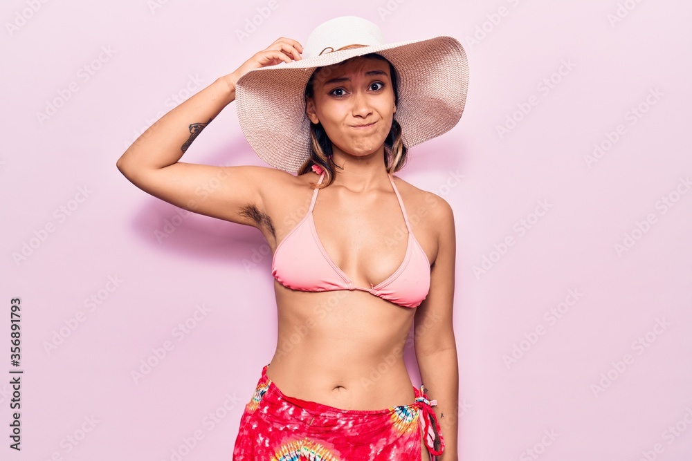 Young woman wearing bikini and hat confuse and wonder about question. uncertain with doubt, thinking with hand on head. pensive concept. Young woman wearing bikini and hat confuse and wonder about question. uncertain with doubt, thinking with hand on head. pensive concept.