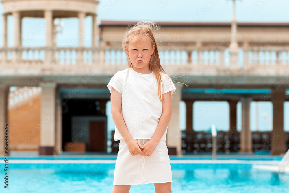 Portrait of a sad little girl standing by the pool. Concept of expressions and emotions