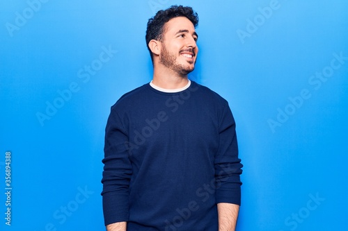 Young hispanic man wearing casual clothes looking away to side with smile on face, natural expression. laughing confident.