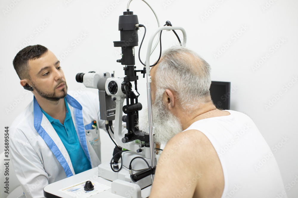 Doctor Optometrist examining bearded senior man eyes with special eye equipment. Doctor Optometrist examining bearded senior man eyes with special eye equipment.