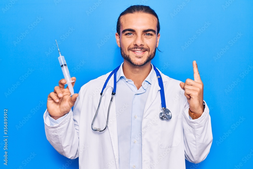 Young handsome man wearing doctor stethoscope holding syringe smiling with an idea or question pointing finger with happy face, number one Young handsome man wearing doctor stethoscope holding syringe smiling with an idea or question pointing finger with happy face, number one