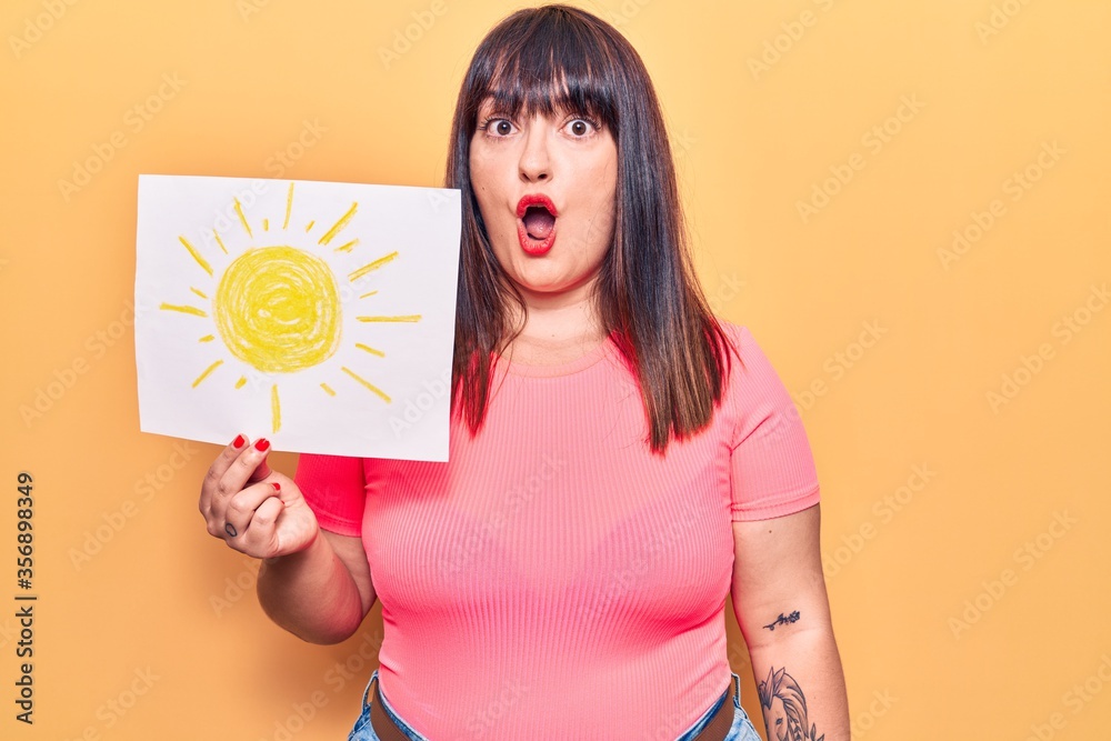 Young plus size woman holding sun draw scared and amazed with open mouth for surprise, disbelief face Young plus size woman holding sun draw scared and amazed with open mouth for surprise, disbelief face