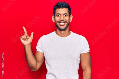 Young latin man wearing casual clothes smiling happy pointing with hand and finger to the side