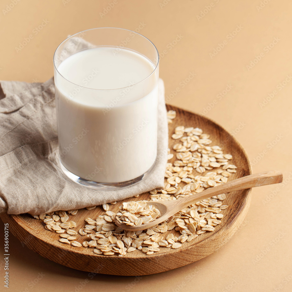 Oat milk in a glass on a wooden plate on a brown background. Milk substitute, milk for vegetarians. Copy space. Oat milk in a glass on a wooden plate on a brown background. Milk substitute, milk for vegetarians. Copy space.