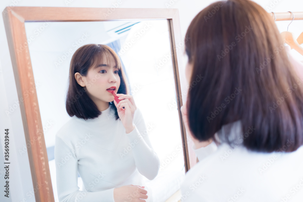 Asian woman make up with cosmatic applying lipstick front mirror at home