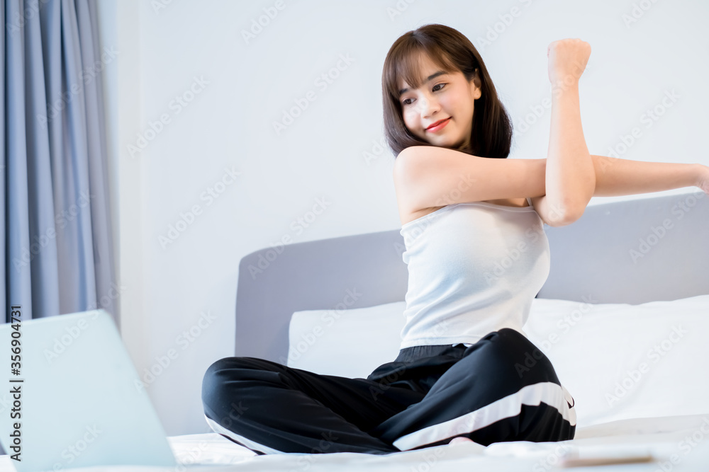 Asian woman stretching exercising on bed and watching tutorial online