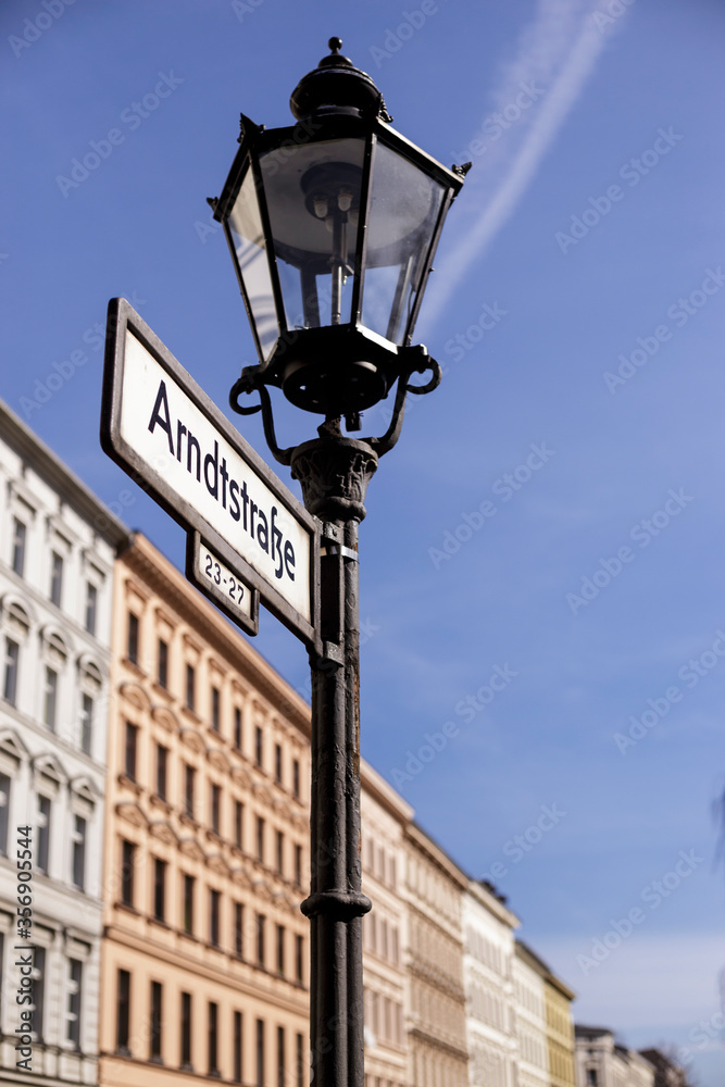 Vertical view of cast iron mast lamp post with baffle lamp and street sign, in the Kreuzberg district of Berlin, with a row of traditional old residential buildings in the background