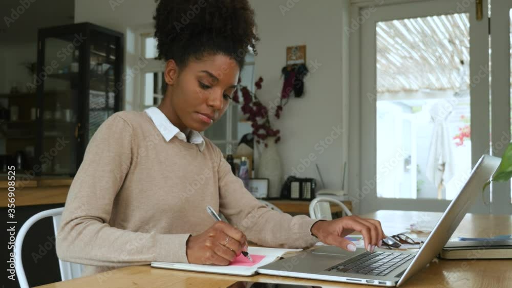 Young mixed race woman with afro working from home in front of laptop