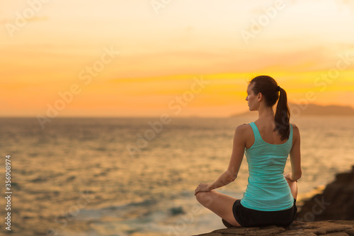 Calm fit relaxed woman meditating on the beach with beautiful view of the ocean during orange sunset sky. Peace and harmony feelings.