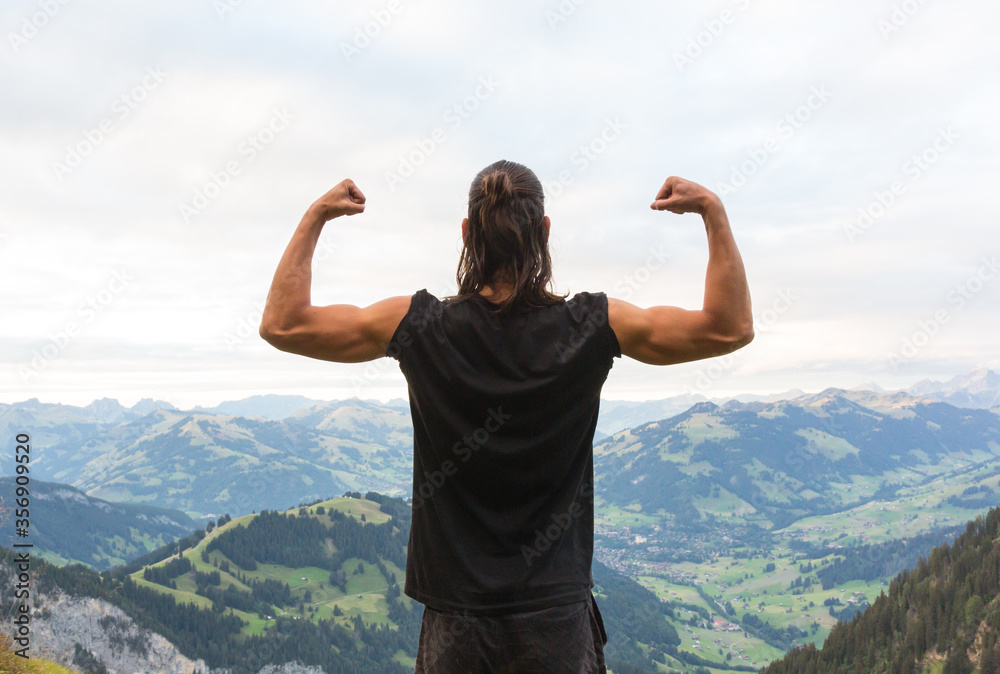 Strength and Power! Strong young muscular hiker man flexing his arms at the top of mountain with scenic landscape view. Strength and Power! Strong young muscular hiker man flexing his arms at the top of mountain with scenic landscape view.