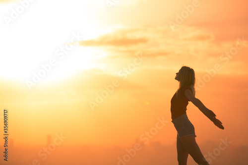 Silhouette of happy healthy spirited woman outstretched with arms up while enjoying the amazing orange sunrise. Peace and well-being concept.