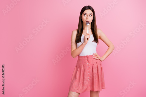 Photo of charming funny lady hold metal table spoon looking tempting empty space dreaming of tasty food dinner wear white singlet dotted skirt isolated pastel pink color background