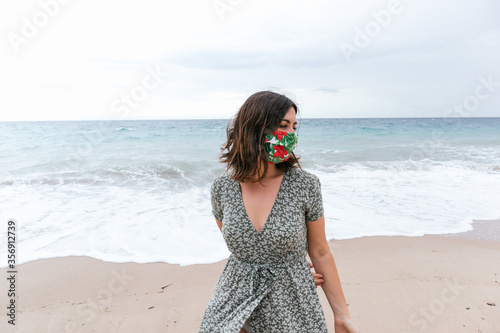 young woman on beach with green dress and mask for covid-19