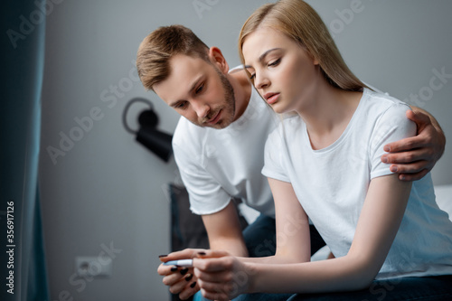 sad man and frustrated girlfriend looking at pregnancy test at home
