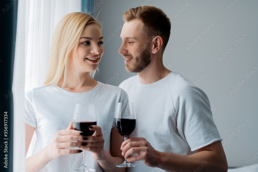 side view of happy man and cheerful woman holding glasses with red wine side view of happy man and cheerful woman holding glasses with red wine