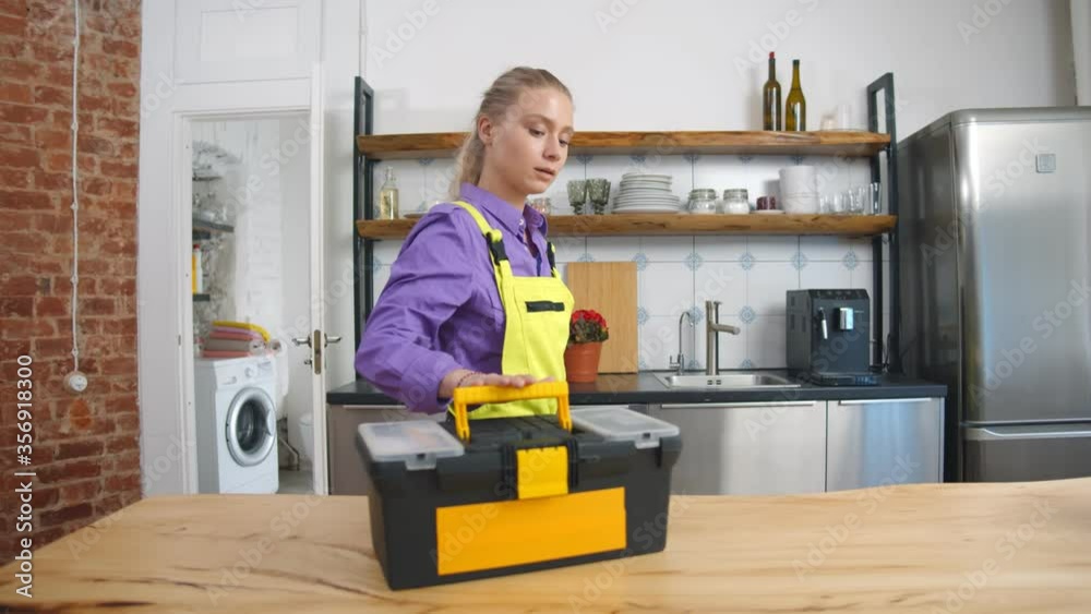 Pretty female plumber examining broken kitchen faucet Pretty female plumber examining broken kitchen faucet
