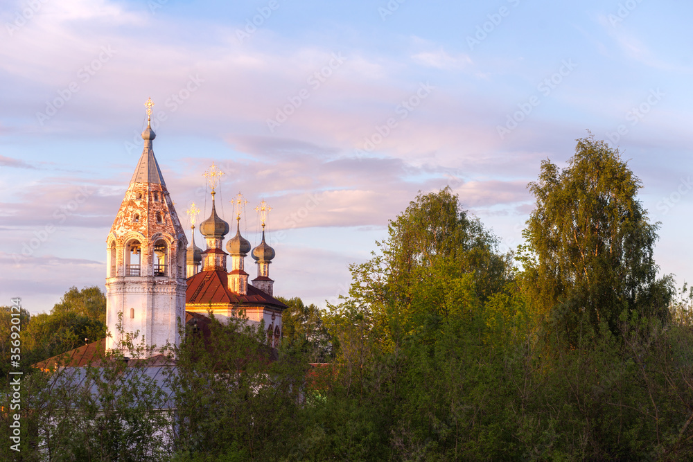 Beautiful summer landscape of the north-western part of Russia. Old Orthodox Church on the banks of a dried river and a wooden bridge over the river. Ustyuzhna, Vologda region. Province of Russia.