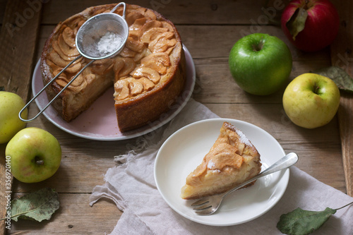 Pie with apple cream filling, apples and dishes on a wooden background. Rustic style.