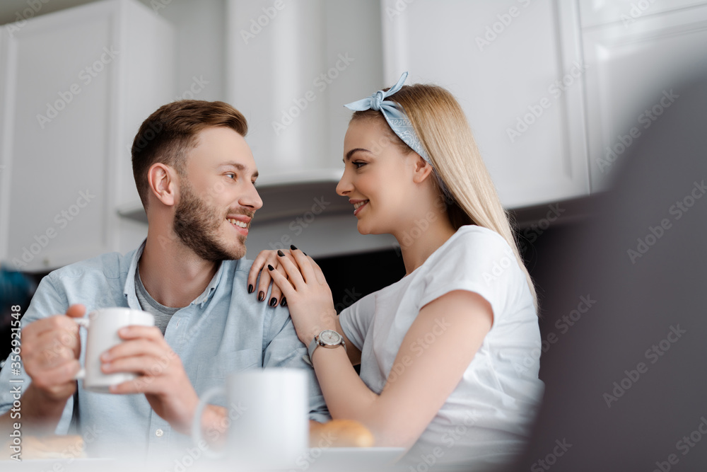 selective focus of beautiful girlfriend and handsome boyfriend looking at each other in kitchen